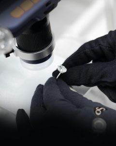 Close-up of a jeweler examining a diamond ring with a microscope and gloved hands.